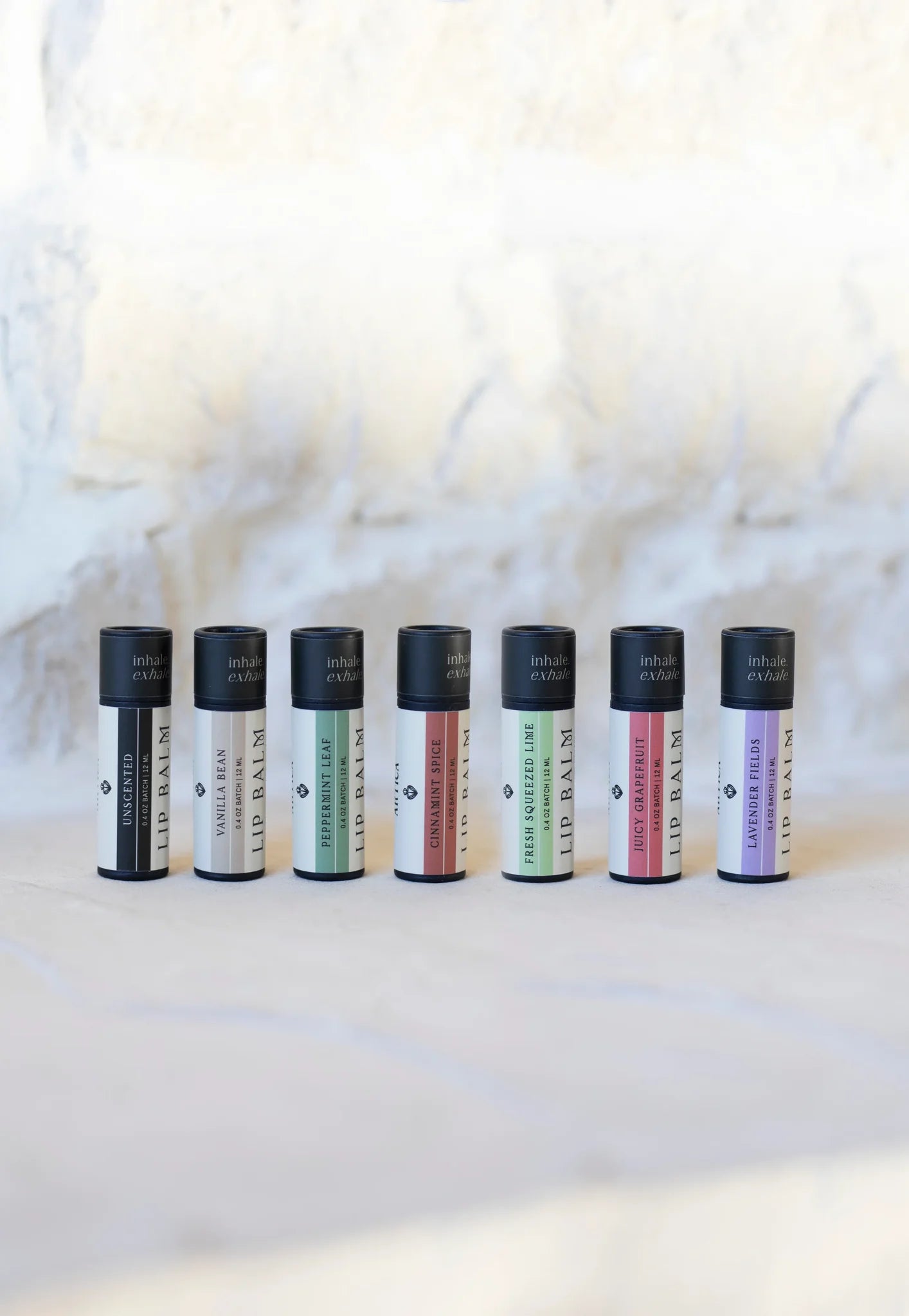 Complete lip balm collection displayed in a row: Unscented, Vanilla Bean, Peppermint Leaf, Cinnamon Spice, Fresh Squeeze Lime, Juicy Grapefruit, and Lavender Fields.